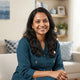 A friendly South Asian woman smiling for a customer testimonial portrait in a modern, bright home setting.