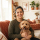 A smiling, diverse pet owner portrait in a sunlit room with warm terracotta and burnt sienna home decor.